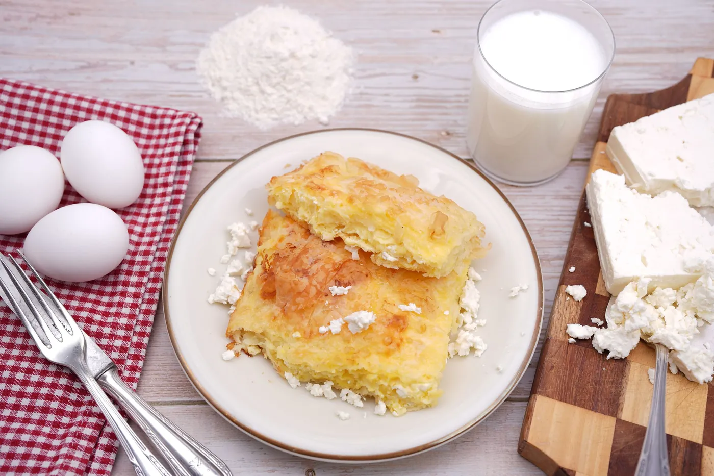 Komadi gibanice na tanjiru, oko njih jaja, brašno, mleko i beli sir
